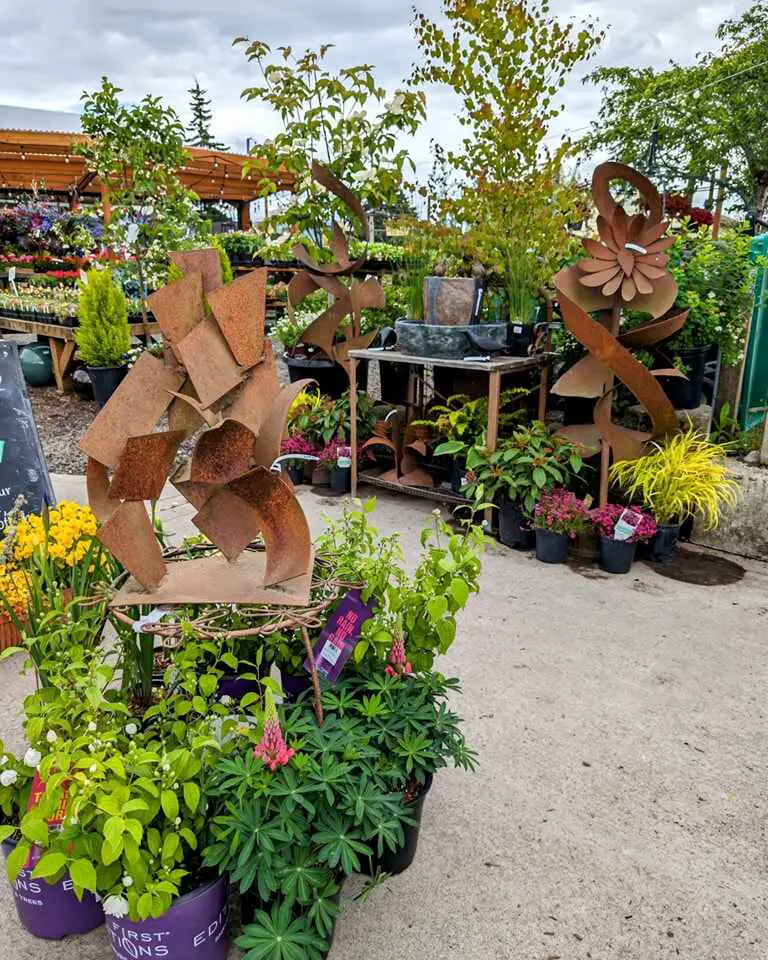 Metal garden sculptures surrounded by potted plants and colorful flowers in a garden center