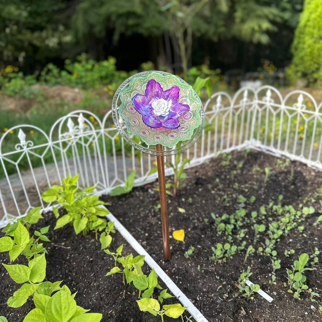 Colorful glass garden stake with a floral design in a garden bed.