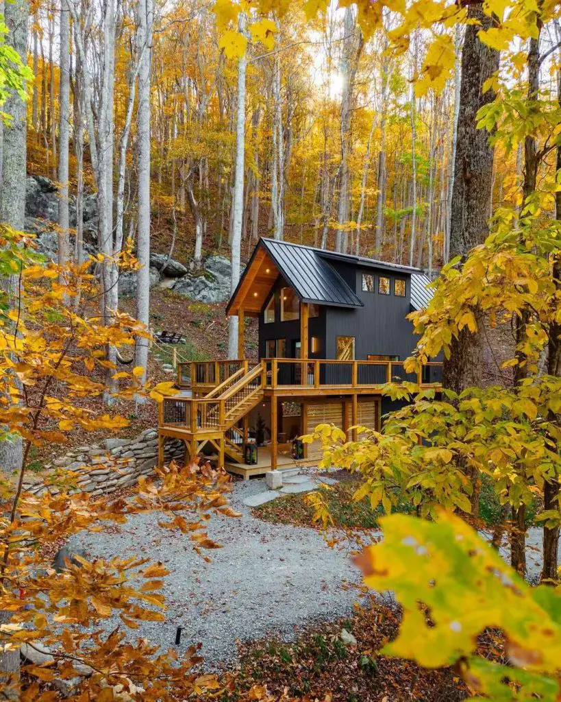 Modern cabin surrounded by autumn foliage with a wooden deck and gravel path