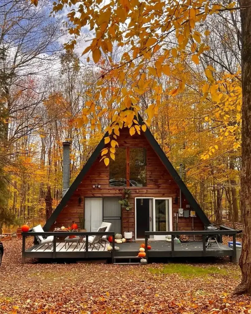 A-frame cabin surrounded by golden autumn leaves and harvest decor