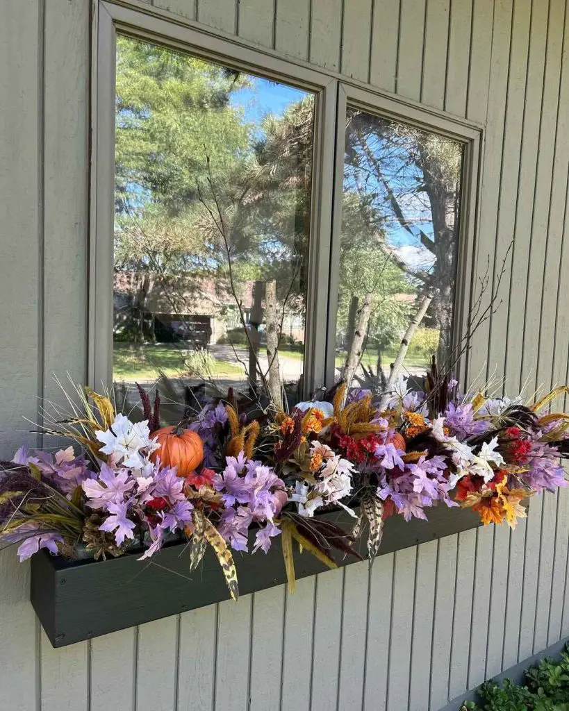 Colorful autumn floral arrangement in a window box with a small pumpkin and natural accents