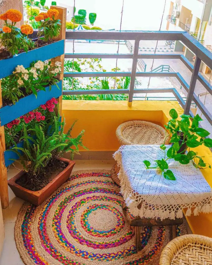 Balcony with potted flowers, a small table, woven chairs, and a colorful rug
