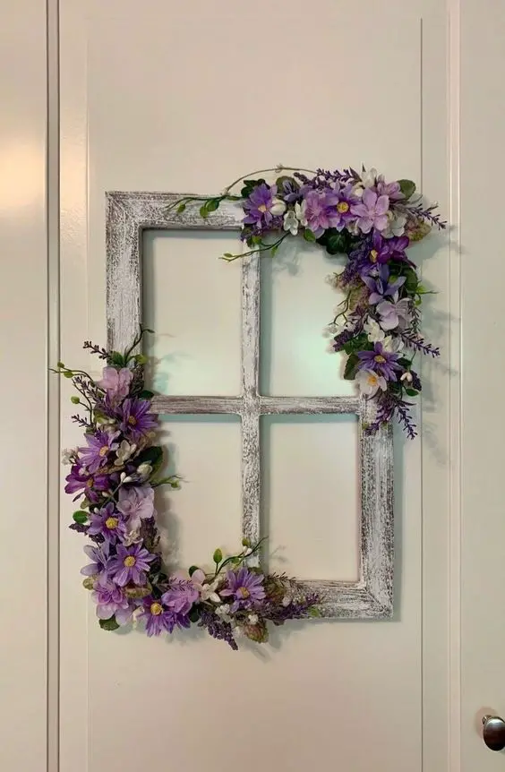 Vintage white window frame decorated with purple and white artificial flowers, hanging on a white door