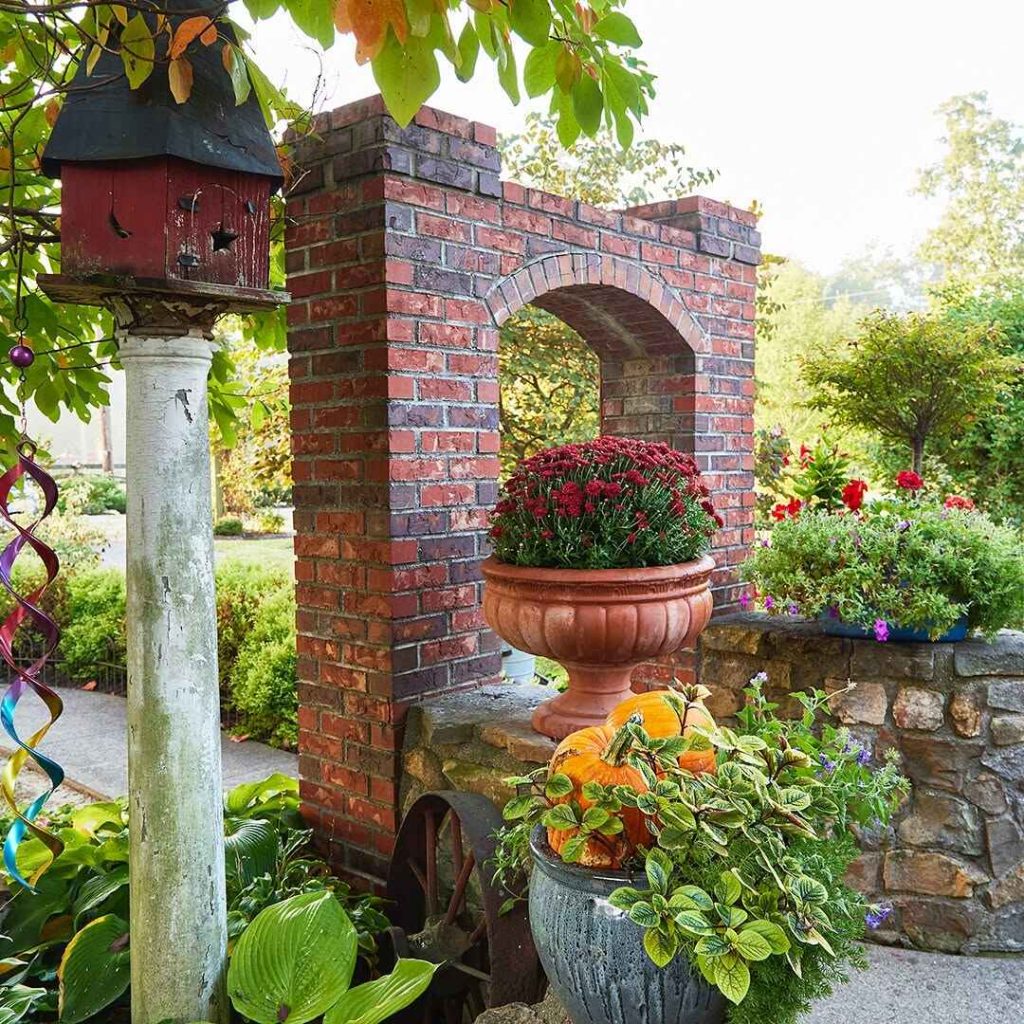 Garden entrance with a brick arch, terracotta pot of flowers, and pumpkins