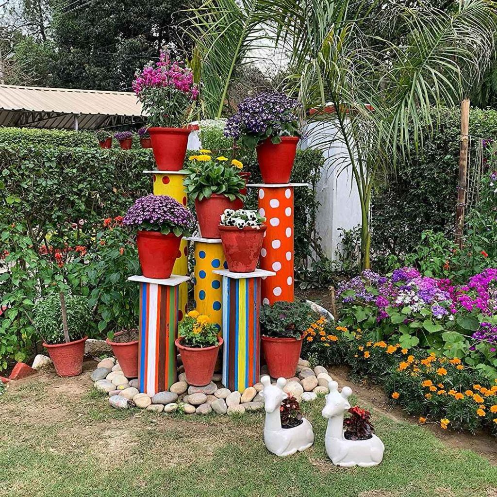 Colorful stacked planters with flowers and whimsical deer planters in a garden