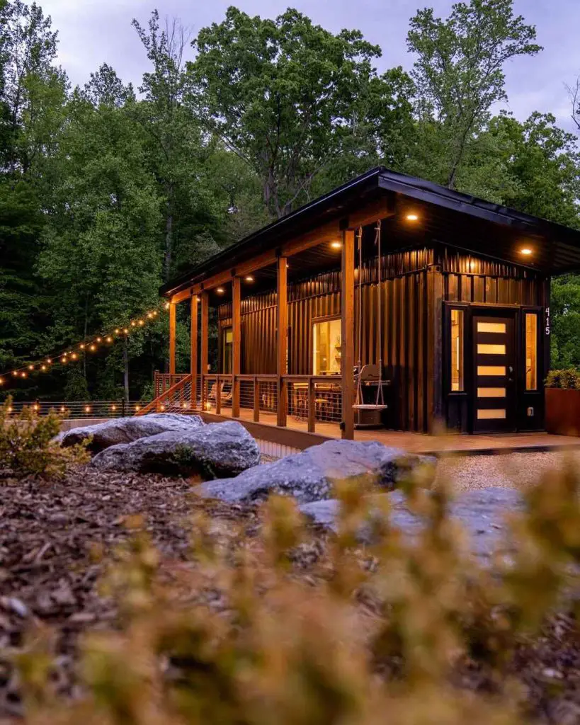 Modern cabin with a welcoming porch surrounded by trees and rocky landscape