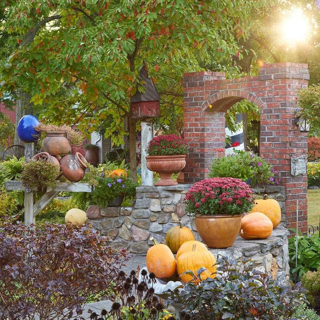 Autumn garden with pumpkins, terracotta pots of flowers, and a brick archway