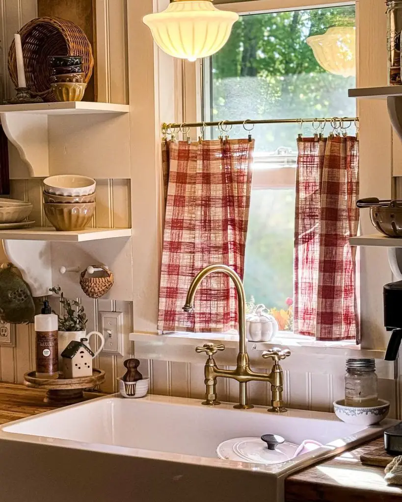 Cozy farmhouse kitchen with sink, gold faucet, and checkered curtains.