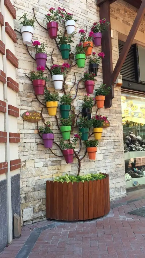 Vertical garden display with colorful pots mounted on a stone wall, resembling a tree, and a wooden planter at the base