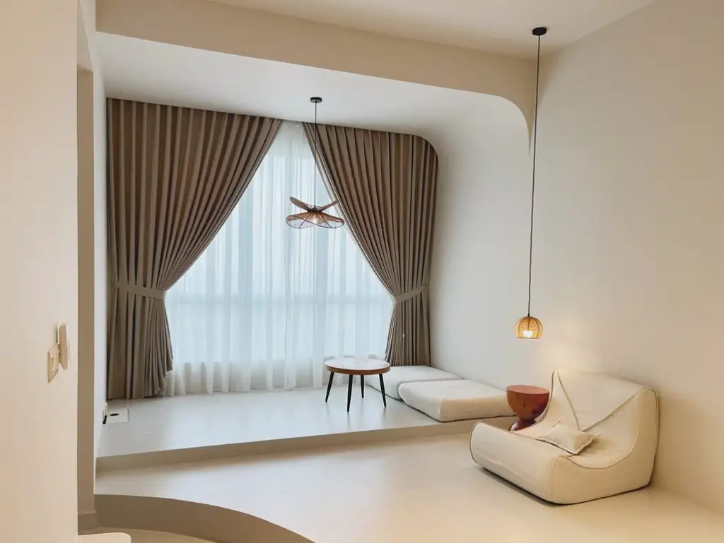 Minimalist living room with curved archway, taupe curtains, white lounge chair, and pendant lights in a neutral color scheme.
