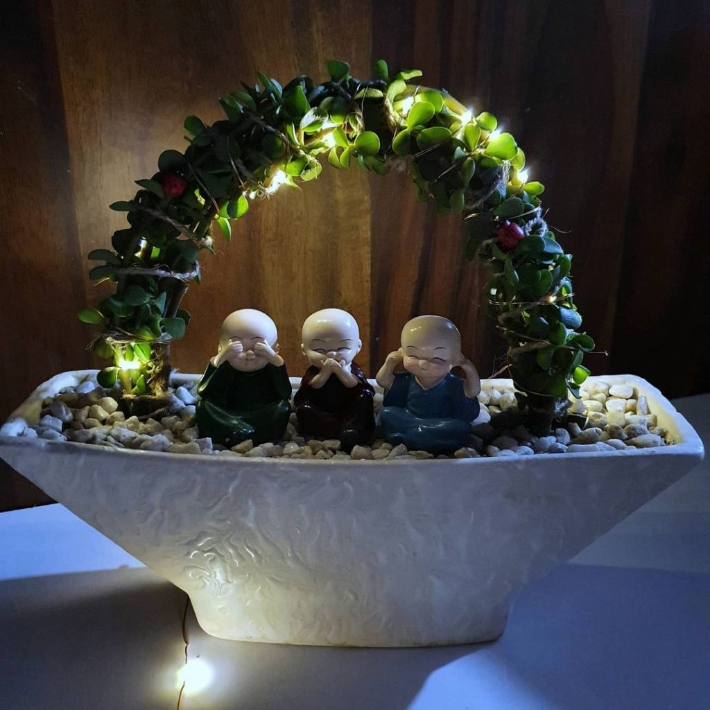 Mini zen garden with lit arch and three monk statues in white bowl