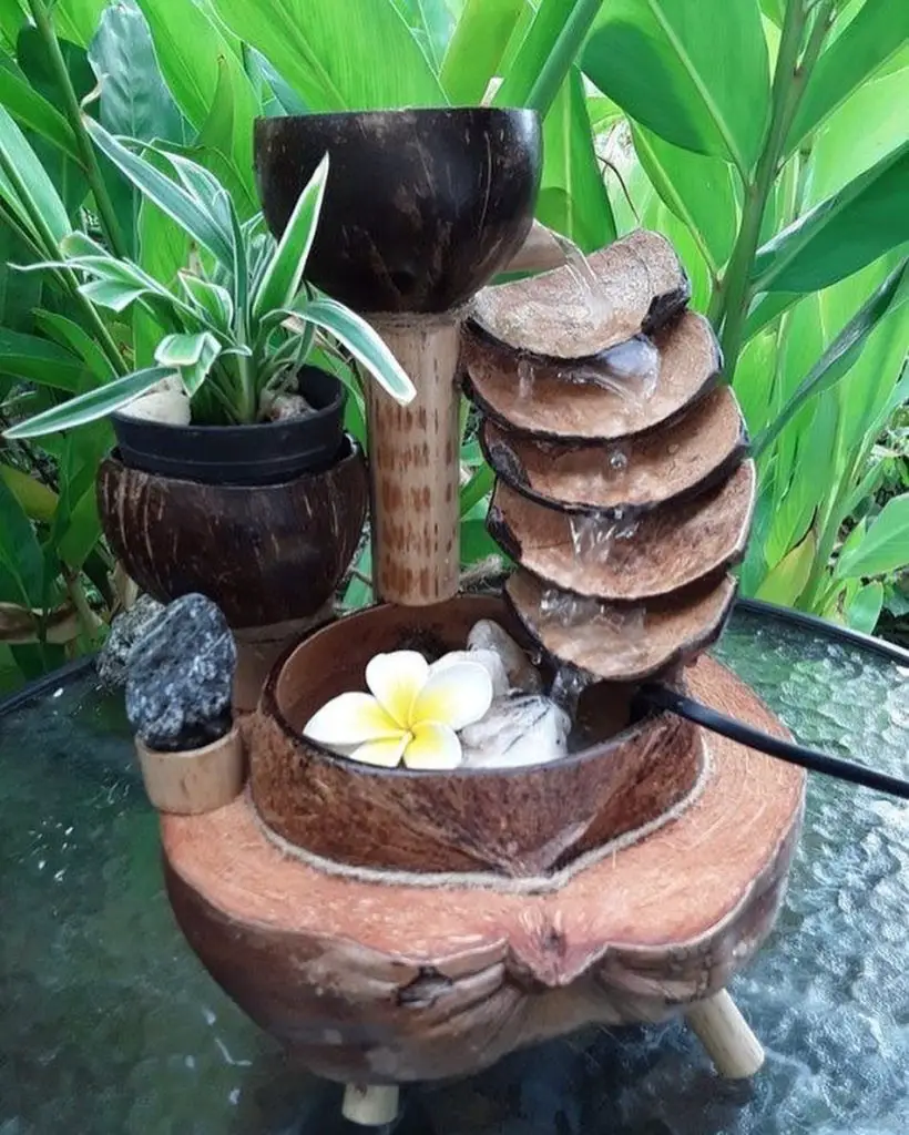Bamboo water fountain with coconut bowls, pebbles, and a white flower.