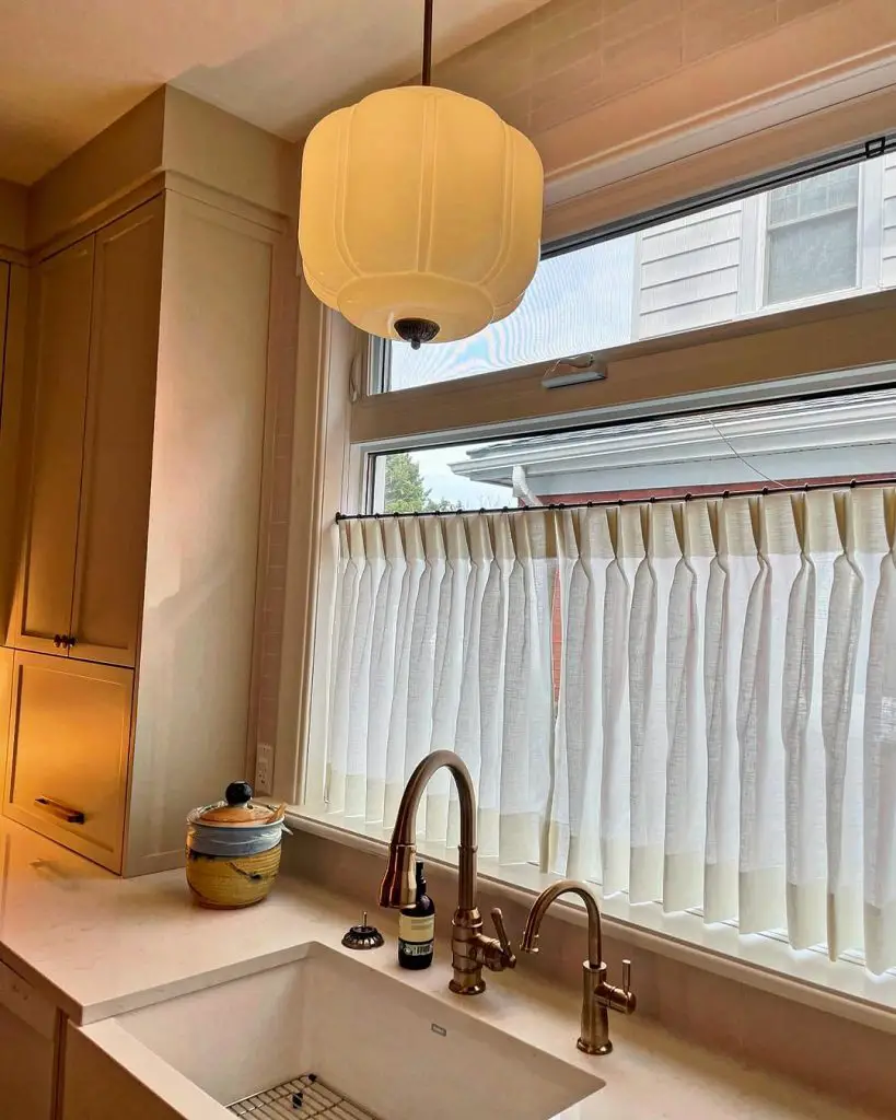 Elegant kitchen with farmhouse sink, bronze faucets, and pleated curtain.