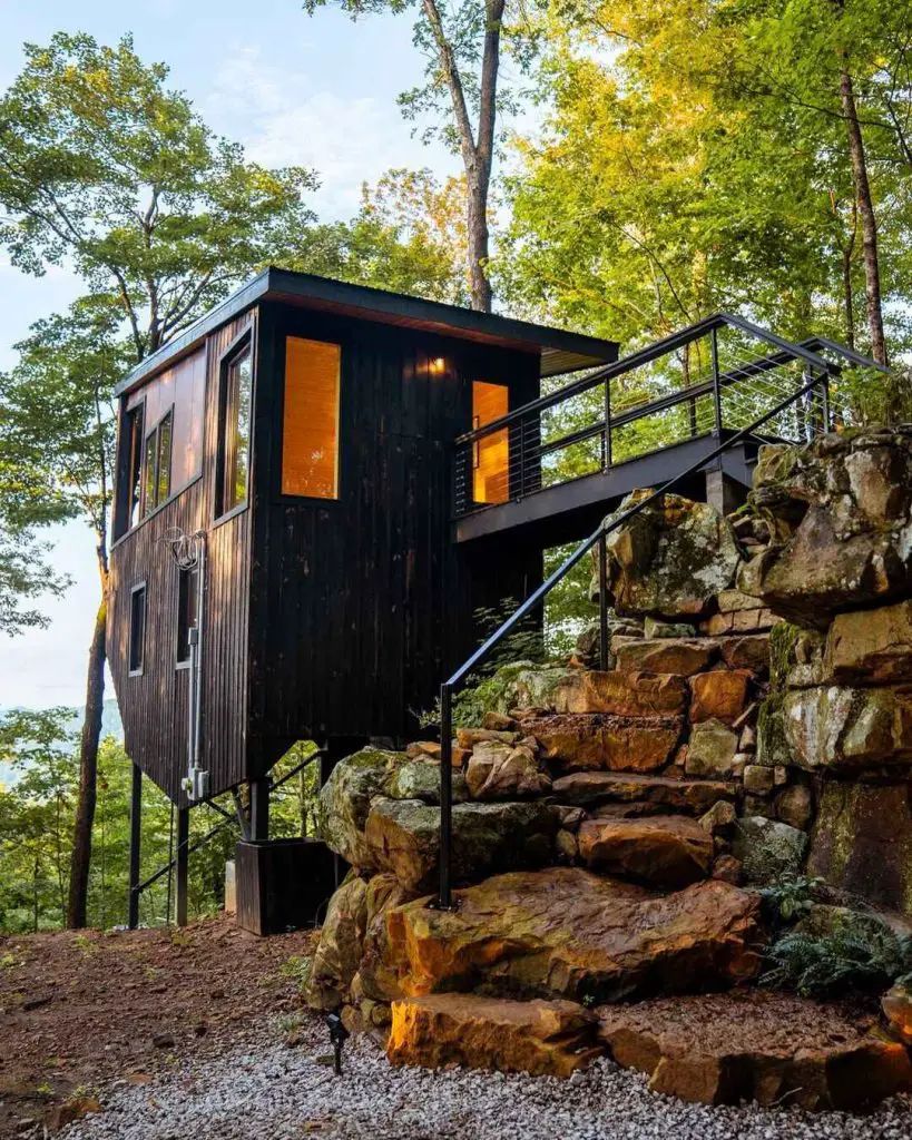 Modern black cabin on a rocky hillside with a staircase surrounded by trees