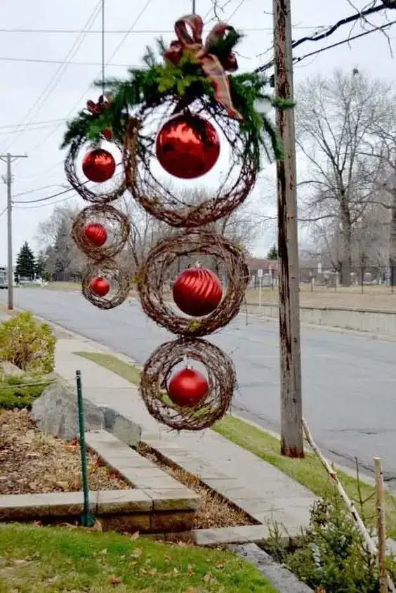 Hanging twig wreaths with red ornaments, cascading down with greenery and a bow at the top, set against a cloudy sky