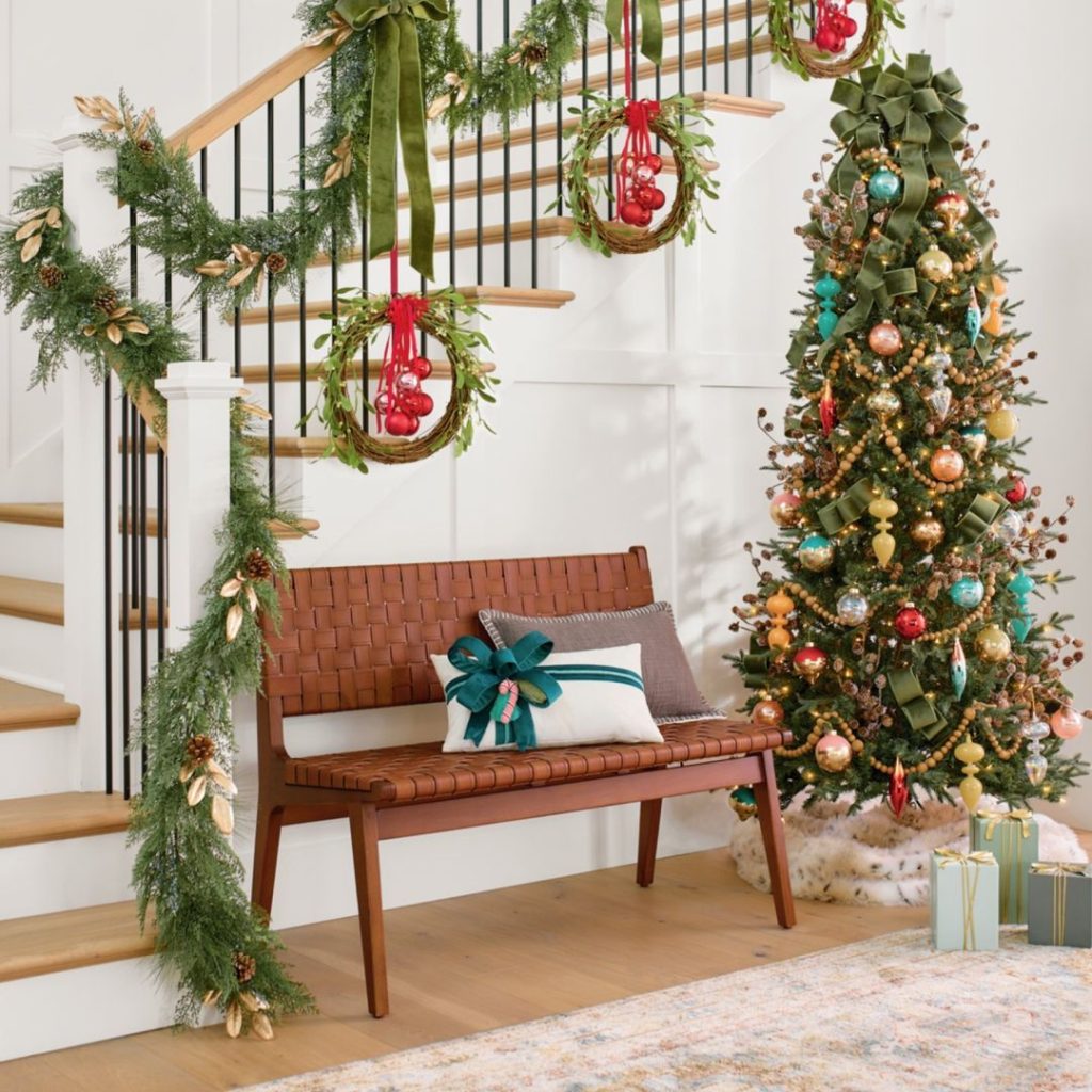 Festive entryway with a decorated staircase, bench, and Christmas tree.