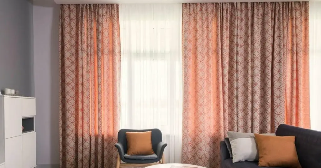 Living room with floor-to-ceiling peach and beige geometric patterned curtains, dark gray sofa and armchair, and white walls.