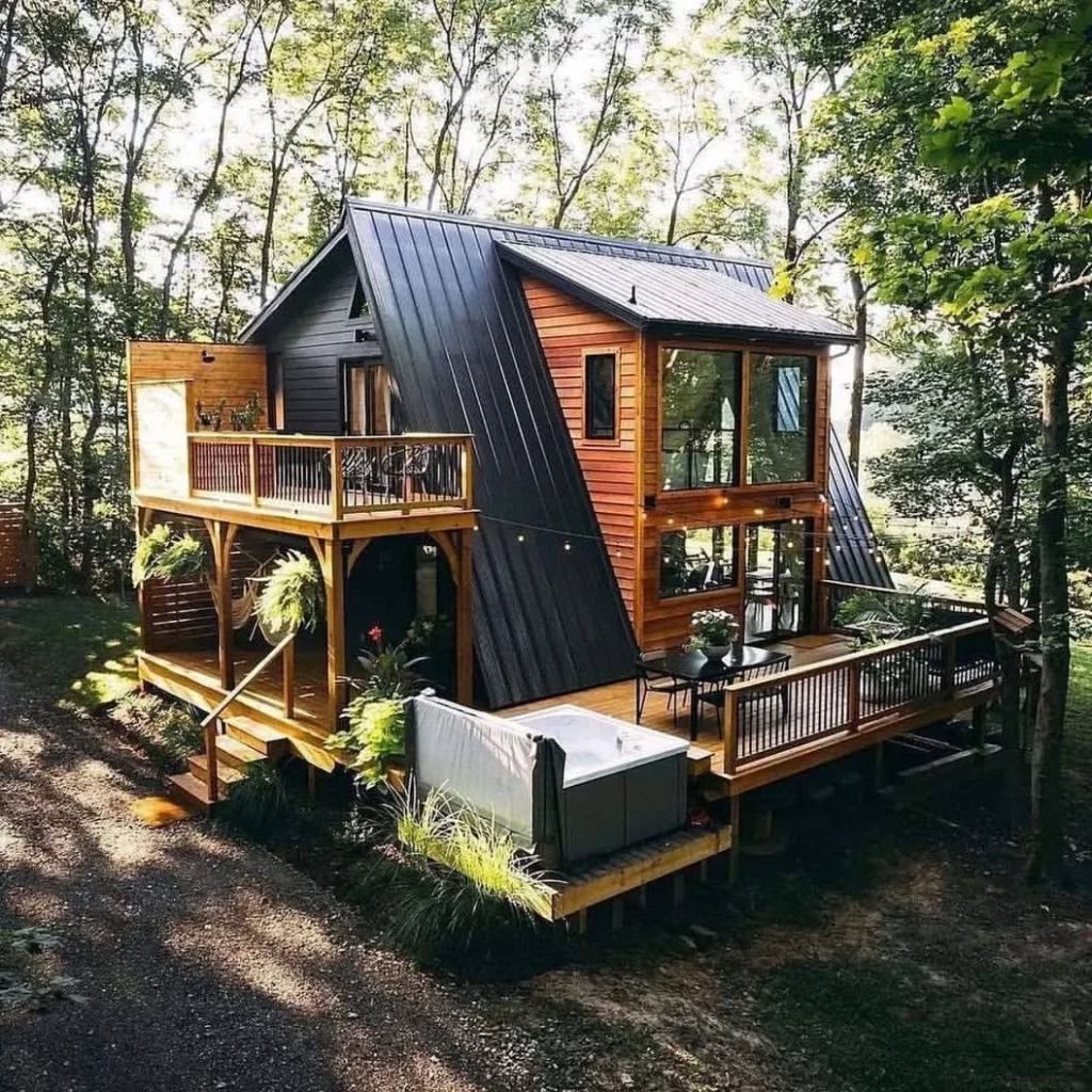 Luxury A-frame cabin with black roof and wooden decks nestled among tall trees
