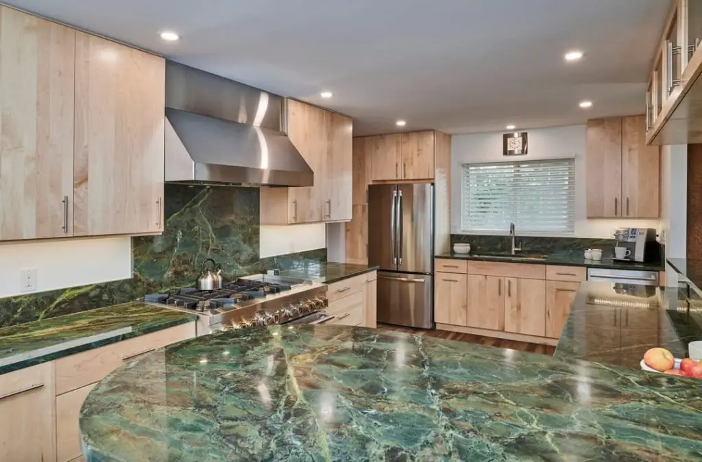Modern kitchen with light wood cabinets, green marble countertops, and stainless steel appliances.