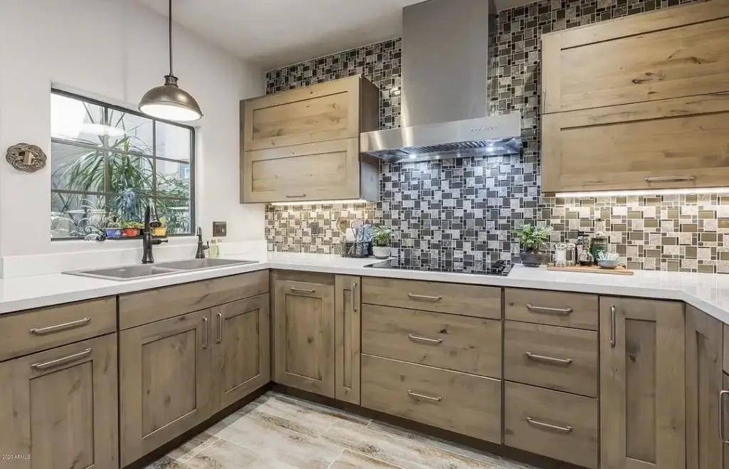 Modern kitchen with natural wood cabinets, textured backsplash, and stainless steel appliances.