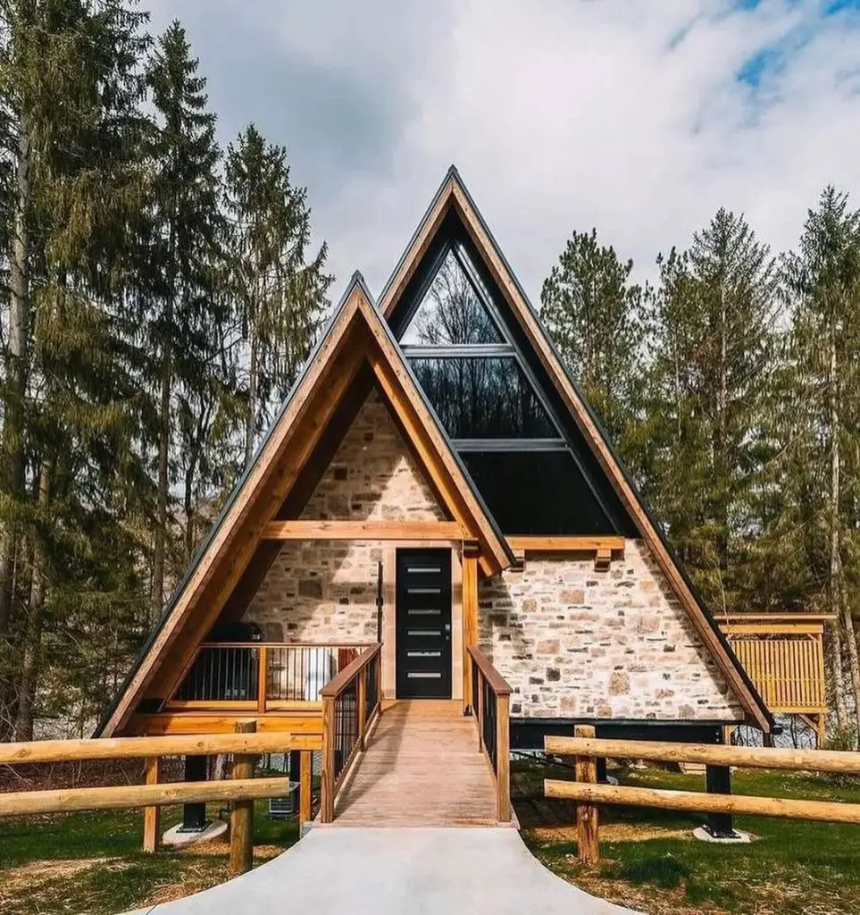 Modern A-frame cabin with stone facade and wooden walkway nestled among pine trees