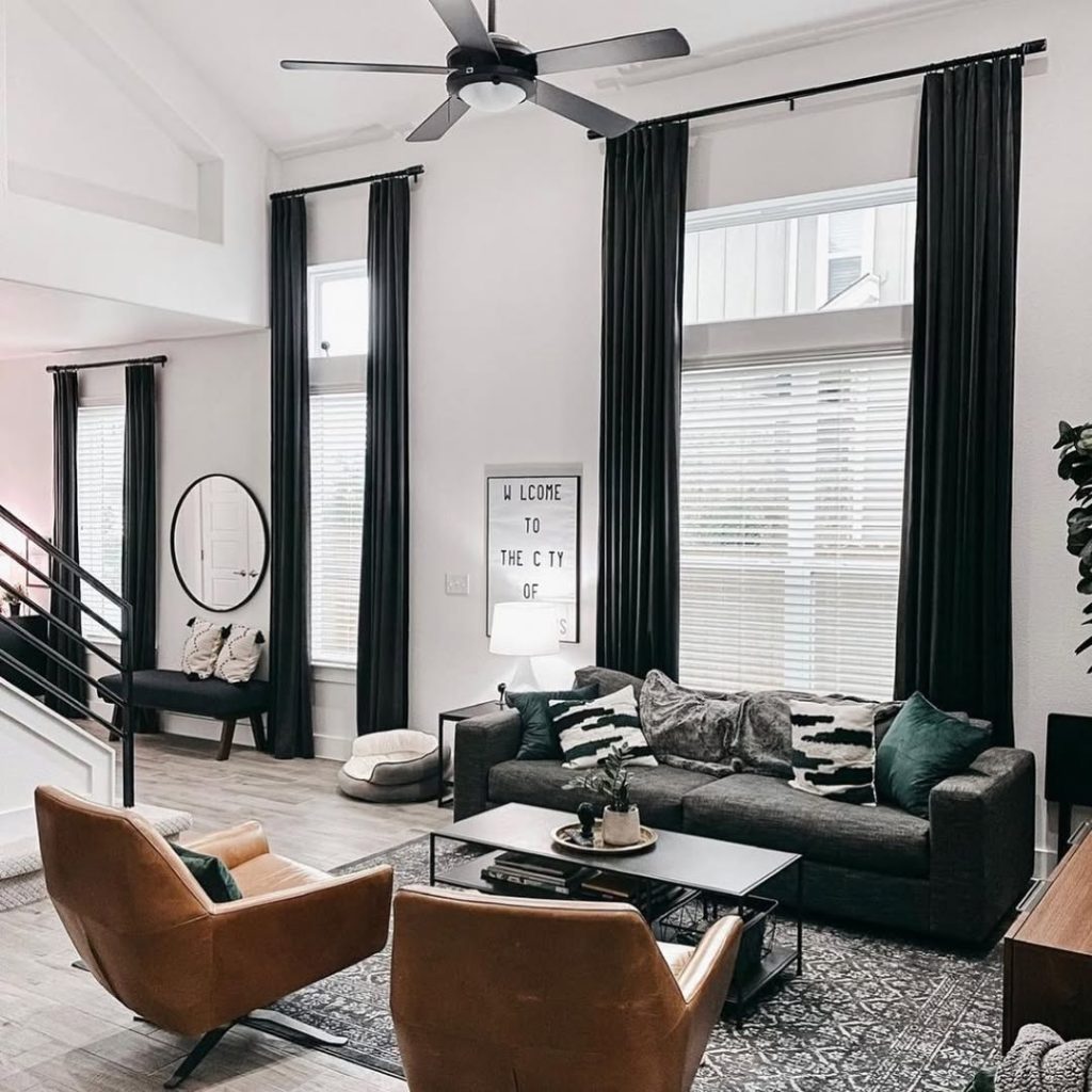 Modern living room with black curtains, gray sofa, and leather chairs in urban setting.