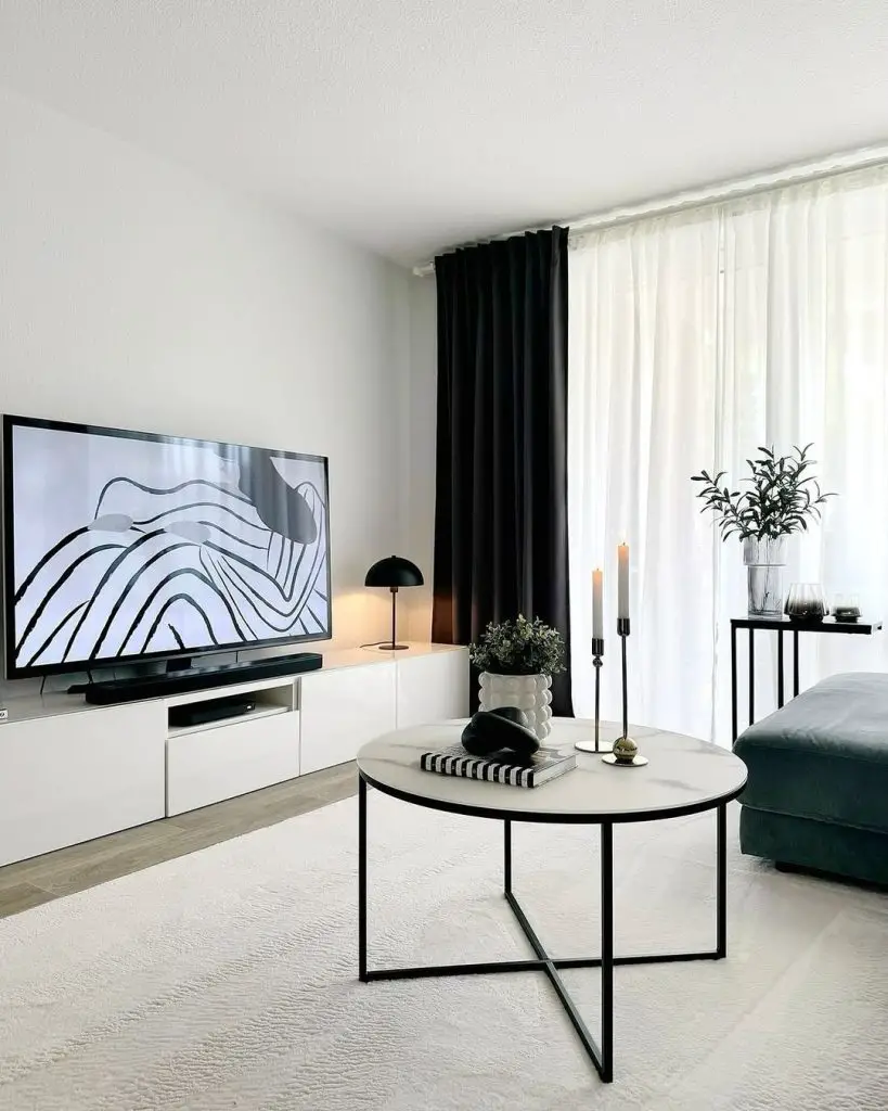 Minimalist living room with black and white decor, featuring a large TV displaying abstract art, contrasting curtains, and a round coffee table.