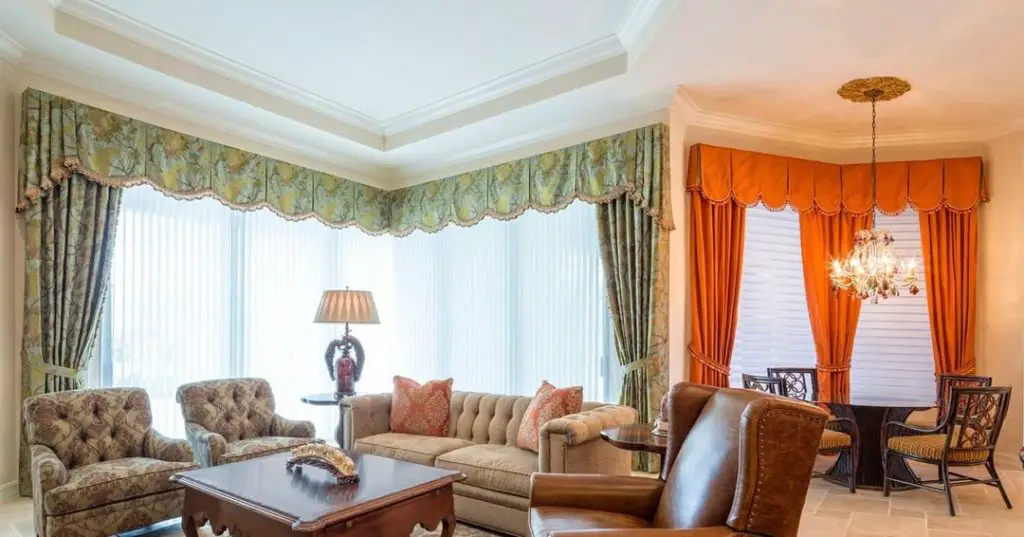 Traditional living room with ornate green and orange curtains, tufted furniture, crystal chandelier, and classic decor elements.