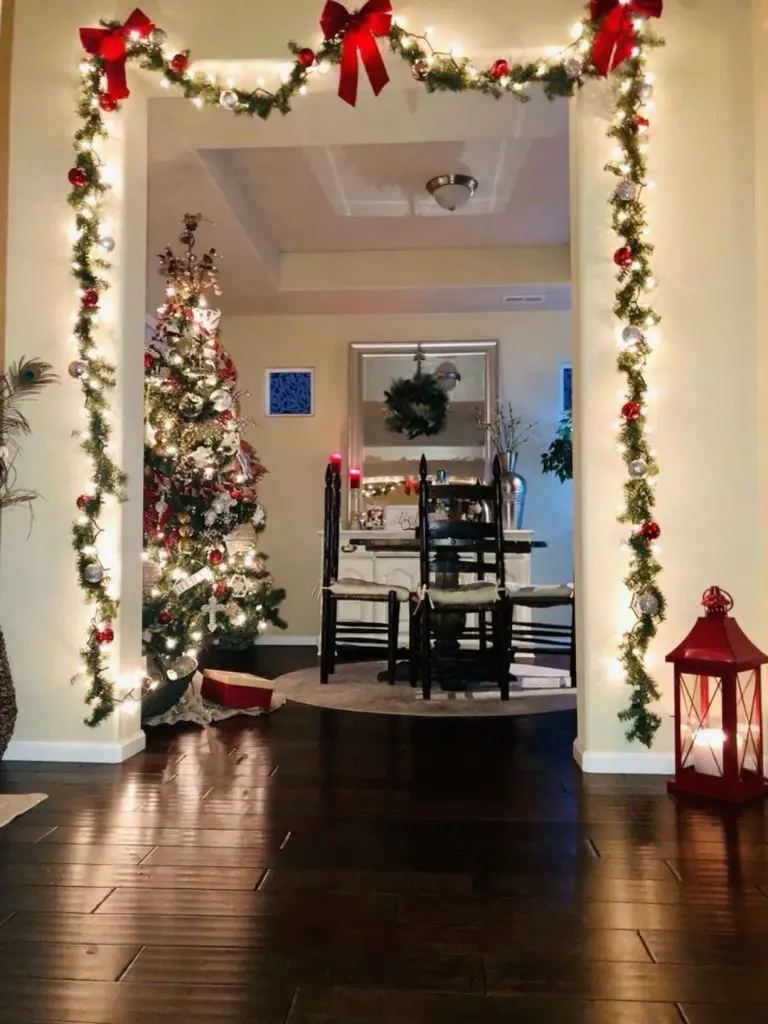 Illuminated archway with red bows garland and Christmas tree creates welcoming holiday entrance