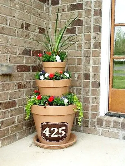 Stacked terracotta pots filled with flowers and greenery, with the house number '425' on the bottom pot, against a brick wall.