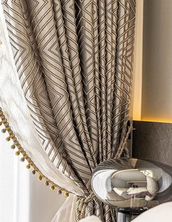Elegant living room curtains with geometric patterns in beige and gold, featuring a pom-pom trim.