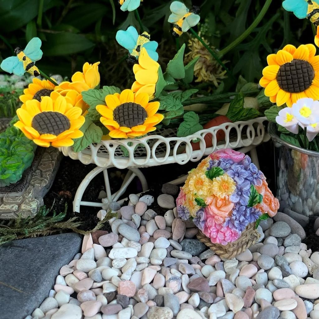 Fairy garden with sunflowers in a cart and colorful flowers.