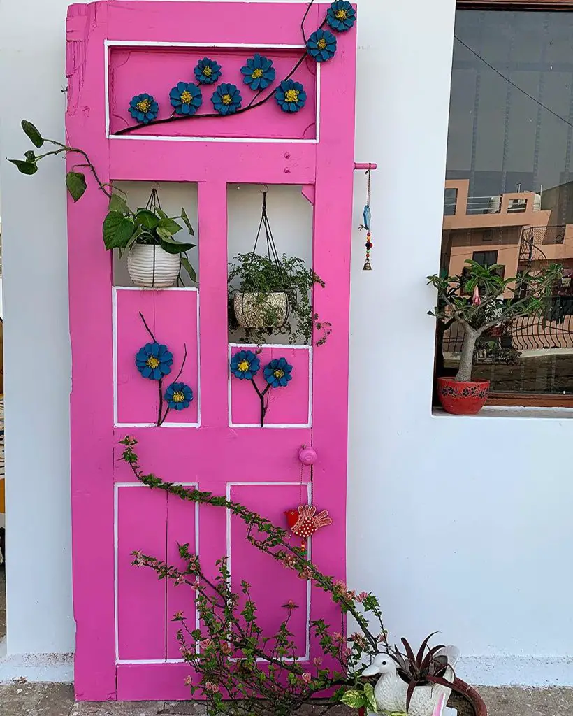 Bright pink door with flowers, hanging plants, and decorative accents