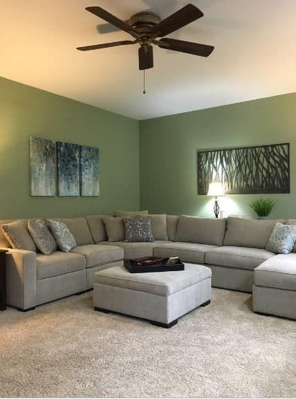 Green walled living room with gray sectional sofa and modern wall art