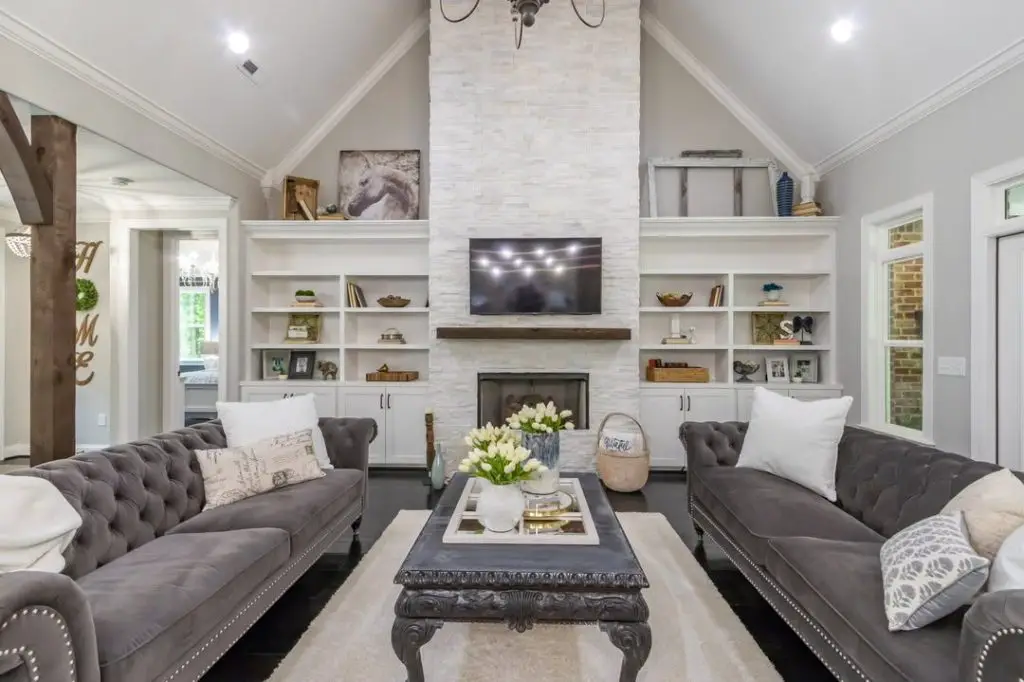 Living room with gray tufted sofas white stone fireplace and built in shelving