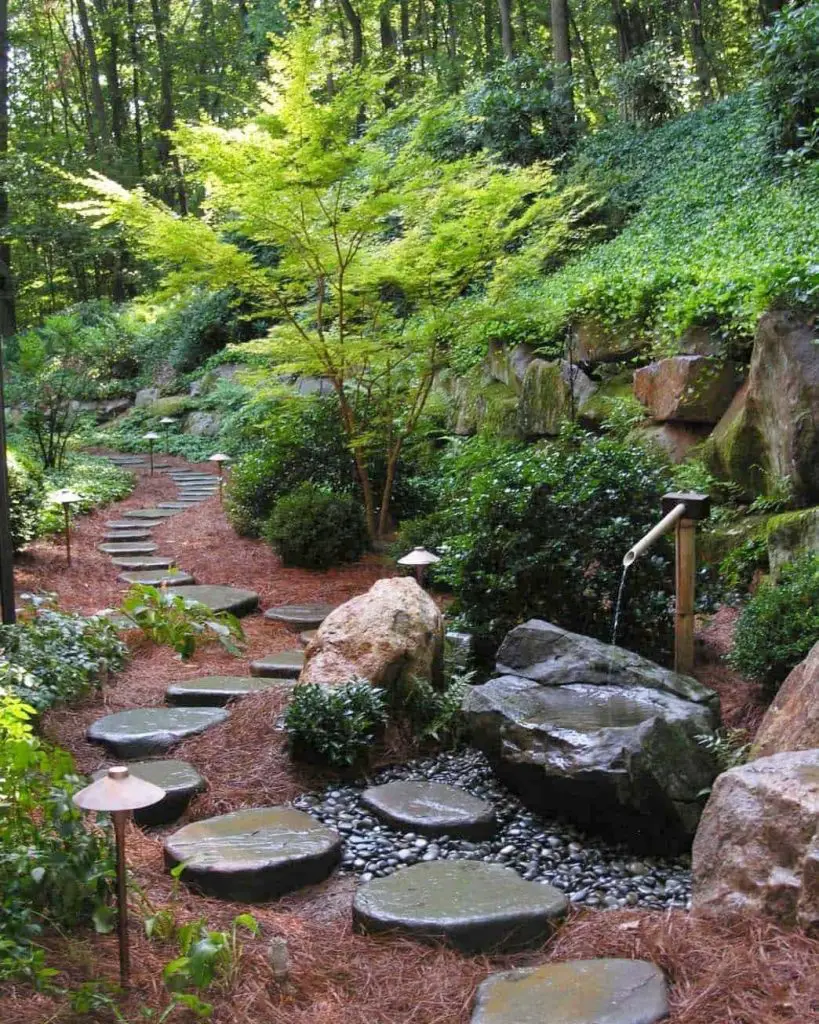 Illuminated stone steps with water feature winding through wooded garden