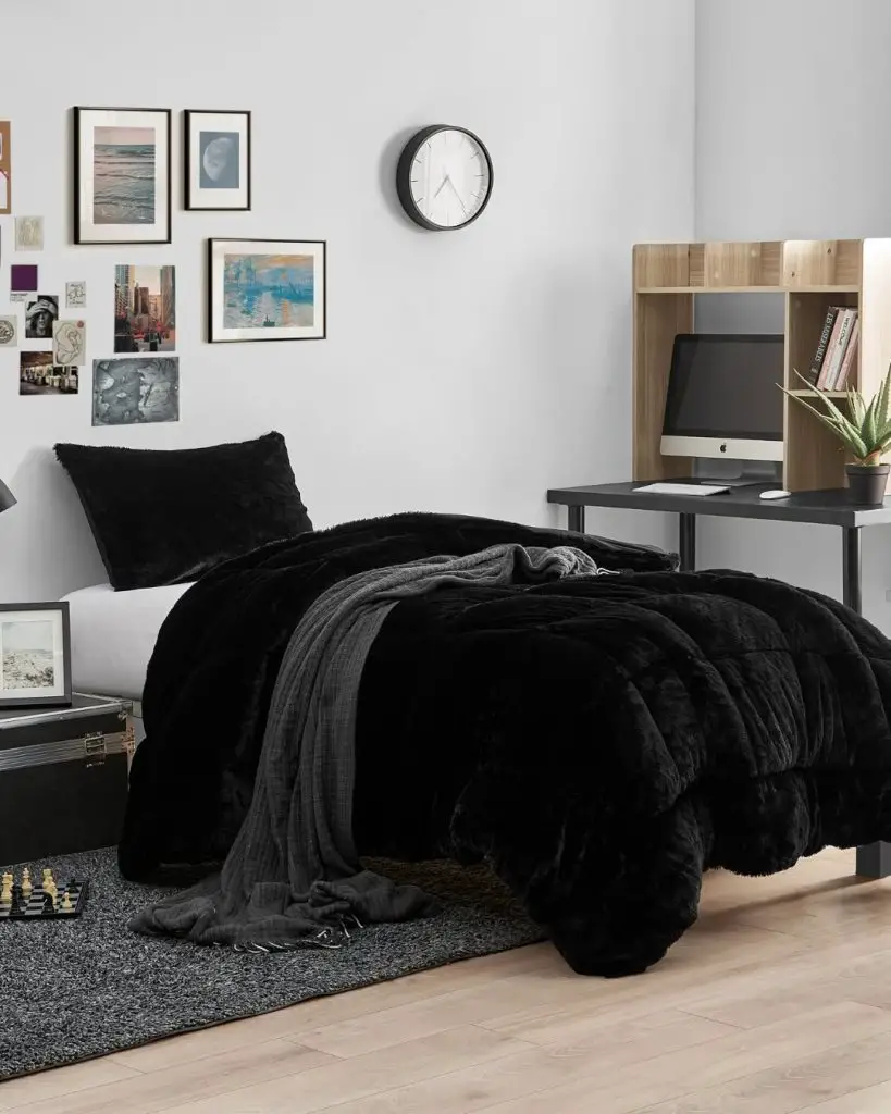 Black plush comforter on twin bed with modern desk setup and gallery wall