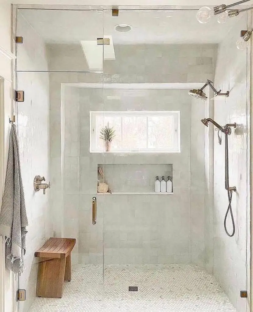 Spacious glass shower enclosure with wooden bench and built-in storage niche