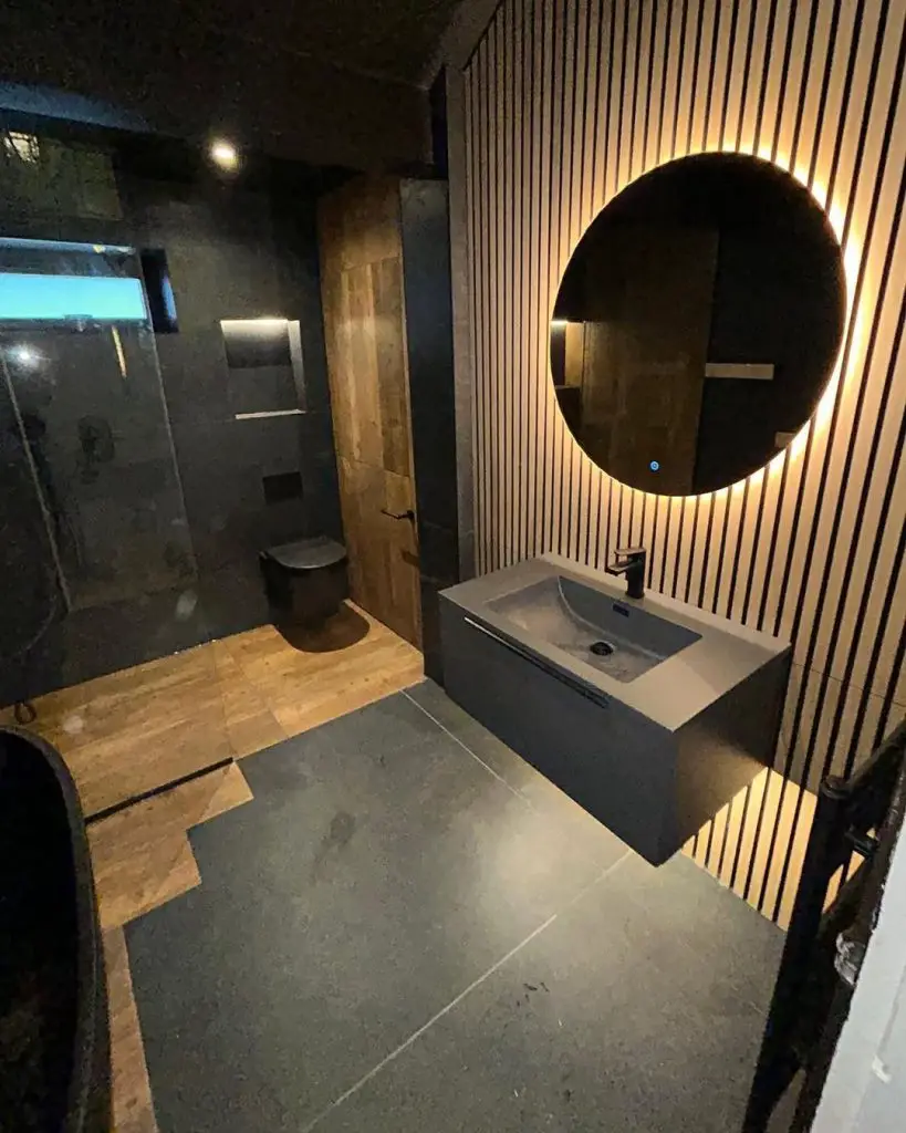 Dark modern bathroom with illuminated mirror and wood accents
