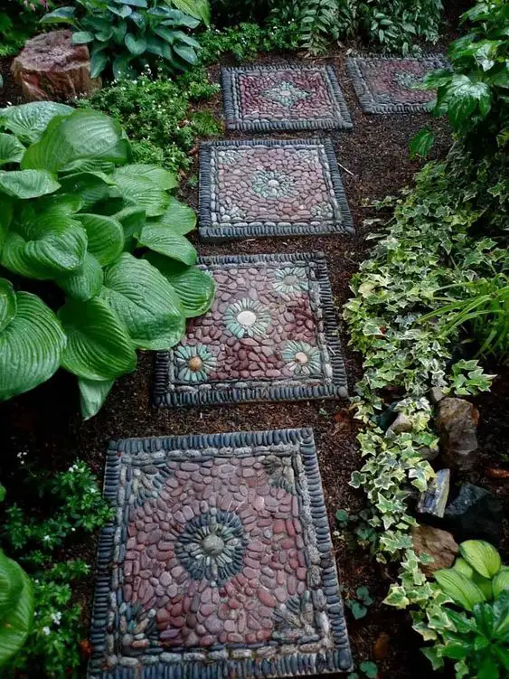 Square stone pavers with pebble mosaic flower designs bordered by plants