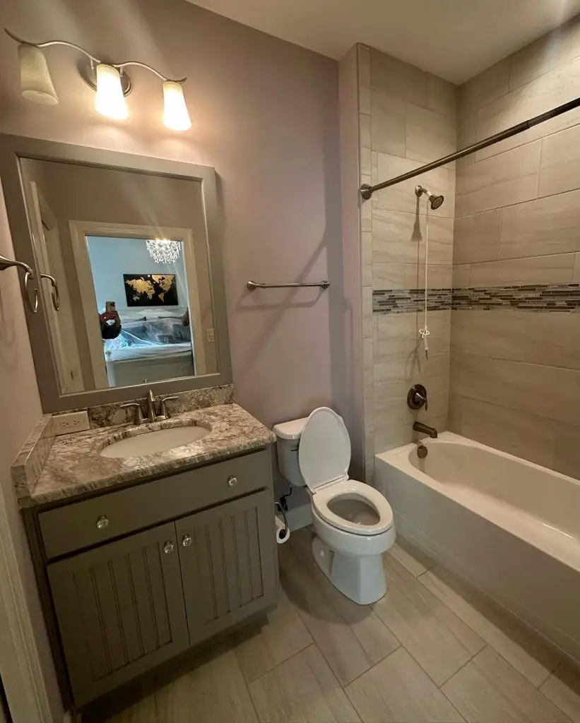 Grey bathroom with marble counter tile shower and framed mirror