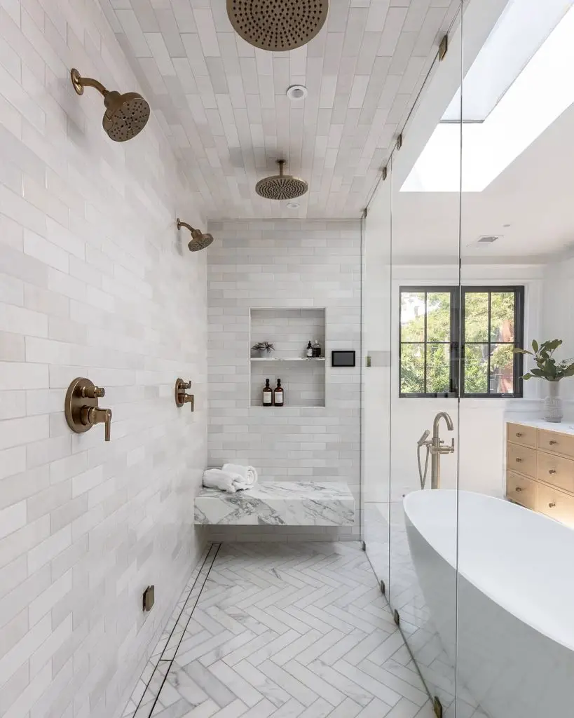 Spacious shower with marble bench and multiple brass fixtures