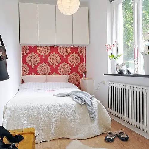 Small bedroom with overhead storage red floral headboard and white bedding