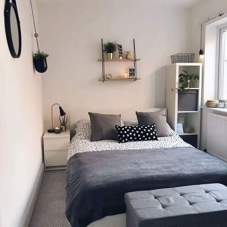 Small bedroom with black and white bedding floating shelves and gray ottoman
