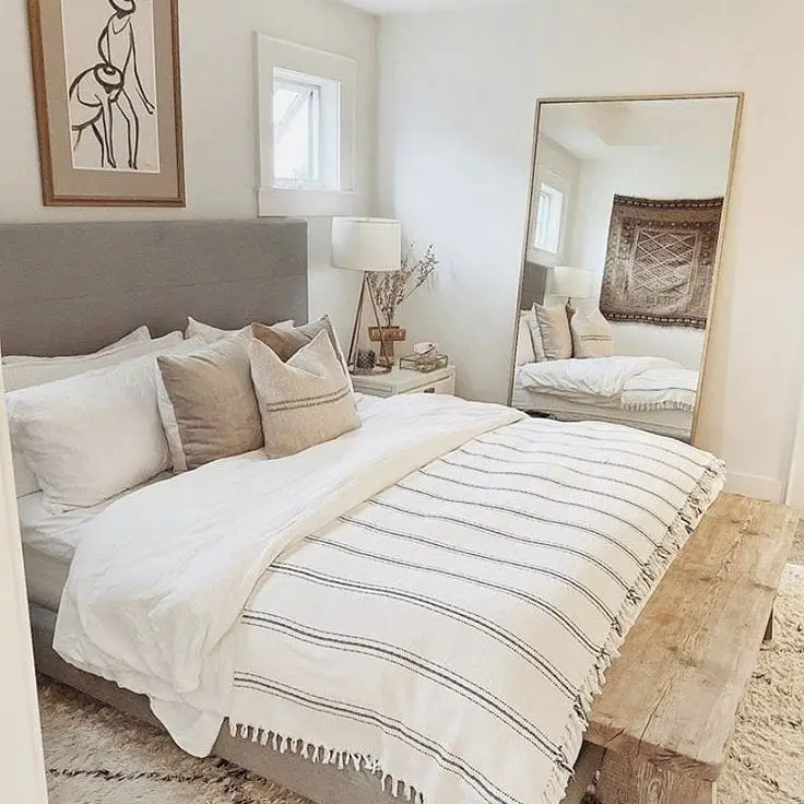 Minimalist bedroom with gray headboard striped throw and leaning mirror