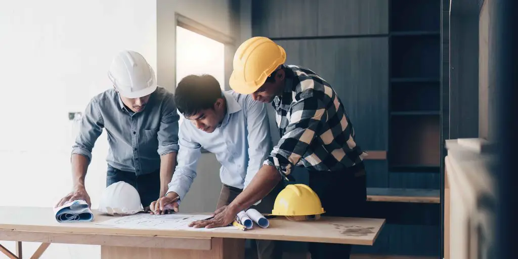 Three professionals reviewing architectural plans at construction site.